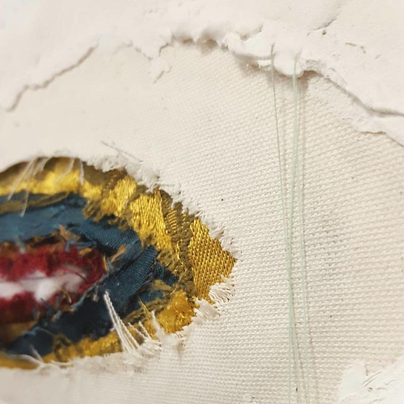 The image is a close-up of a textile artwork with a torn, ragged appearance.