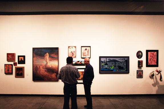 two figures standing in the middle of the gallery, artwork is hung on the walls