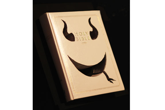 the holy bible with devils horns and smile cut out of the book