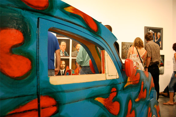 car sculpture in the middle of gallery, artworks on the wall