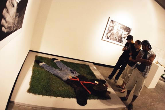 Three people look at an installation work, flattened bearskin with pants and a hat on.
