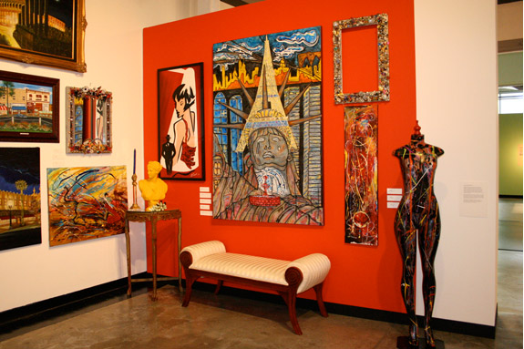 install shot of paintings on red. art wall with a bench and mannequin with splattered paint