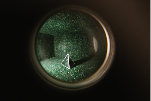 A pyramid on green turf seen through a lens.
