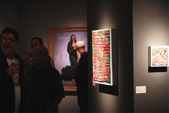 Installation shot of patrons visiting the gallery and artworks lit up in a dark space
