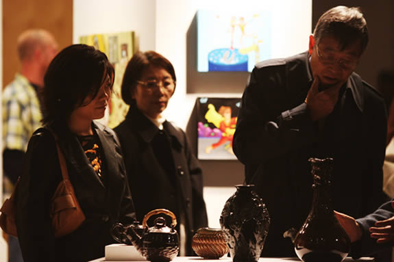 Three guests admiring several ceramic objects