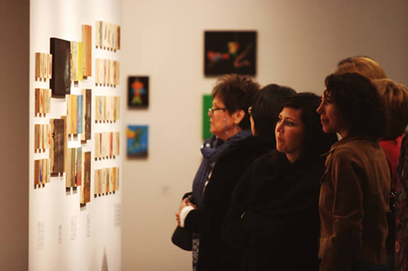 A group of visitors observing various wood panel drawings
