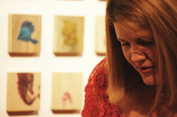 A woman in front of drawings on wood panels.