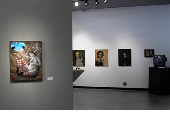 Unnaturally Marvelous On the left wall, a prominent painting features a woman lying on a bed of flowers, with a sky scene visible in the background. The painting has a surreal and dreamlike quality. On the right wall, there are four smaller paintings lined up. They depict various subjects, including a woman in a dress, a stylized figure, a dark portrait, and a framed photograph. In the background, a television monitor is visible on a black stand. It adds a contemporary touch to the gallery space.