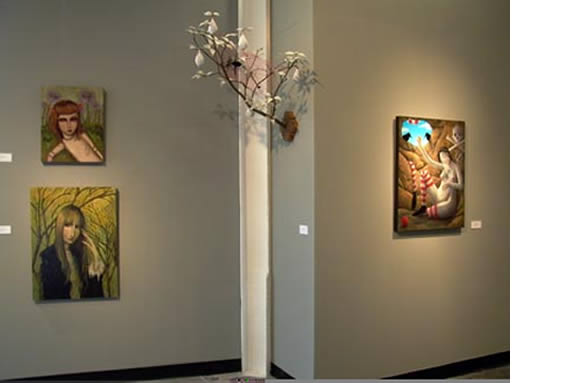 On the left wall, there are two paintings. The first is a portrait of a young woman with red hair, seated in a field of flowers. The second painting features a woman with long, flowing hair, standing amidst a vibrant yellow and green forest. On the right wall, there is a single painting. It depicts a woman lying on a bed of flowers, surrounded by colorful butterflies. The painting has a whimsical and dreamlike quality. A branch with white flowers and leaves is mounted on the pillar, adding a touch of nature to the gallery space. The overall atmosphere of the image is serene and contemplative.