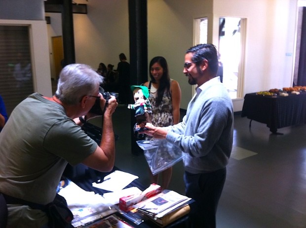 man in foreground photographs man in background as he packs objects on a black cloth covered table.