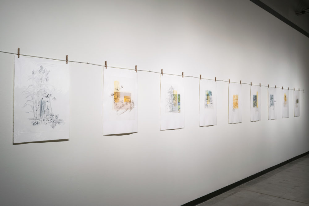 Several paper pieces of various sizes are clipped to the line using clothespins. The artworks appear to be mixed media pieces, possibly including drawing, painting, and collage.