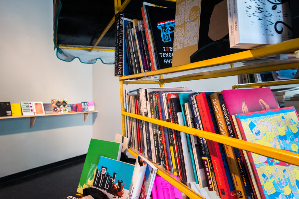 A yellow metal shelving unit is filled with a variety of books, ranging from hardcover novels to smaller paperbacks.