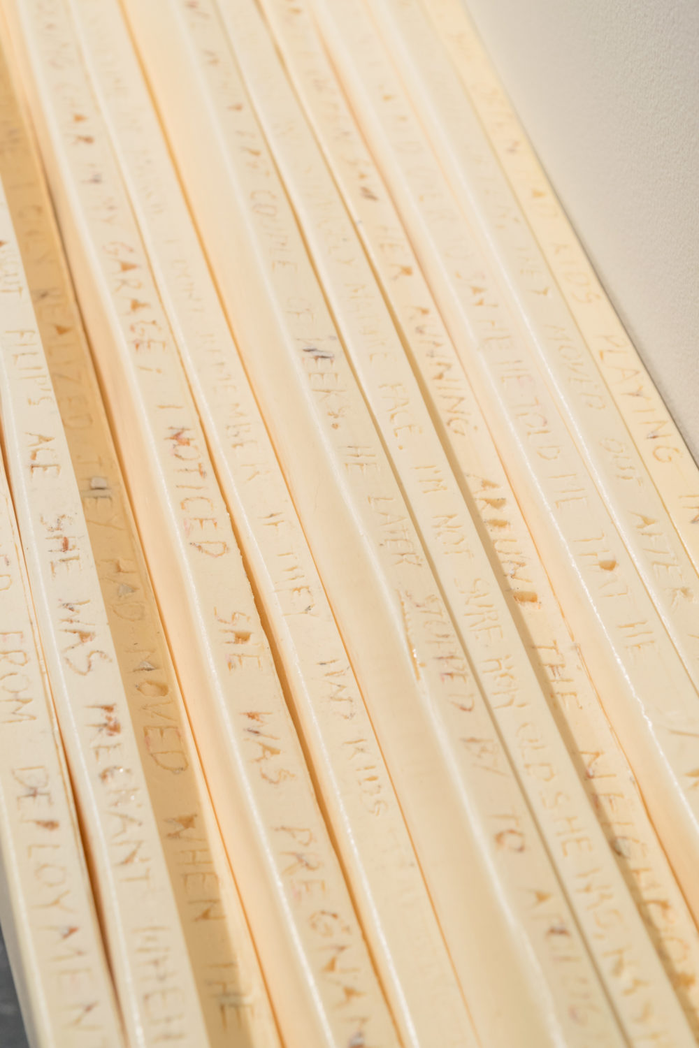 This image depicts a series of long, thin, rectangular objects arranged side by side. Each object is inscribed with a series of letters or words in a vertical orientation. The text is difficult to read in its entirety due to the small size and the angle at which the objects are positioned. However, some words and phrases are partially visible, such as "I INVITED" and "SHE WAS PREGNANT."
