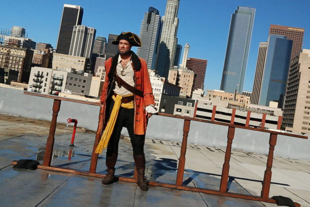 A male pirate stands against a railing