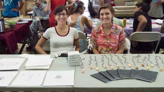 Two people seated selling pendants and prints