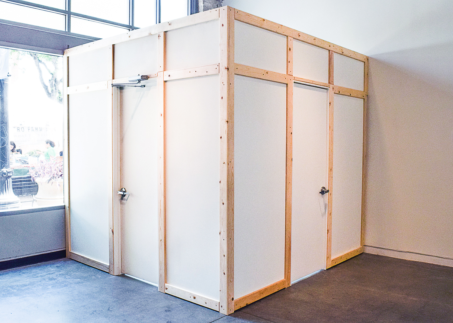 A white, wooden-framed structure occupies a significant portion of the space. It has a door and appears to be a room within a room. Lucas Murgida None of This is Real exhibition