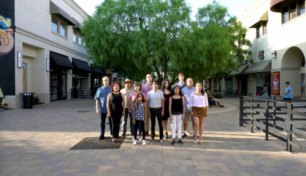 A group of twelve diverse people are standing in a promenade and looking straight to the camera.