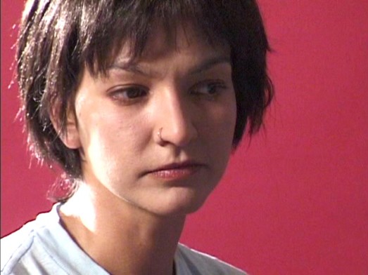 Still from video showing the face of a woman in front of a red background.