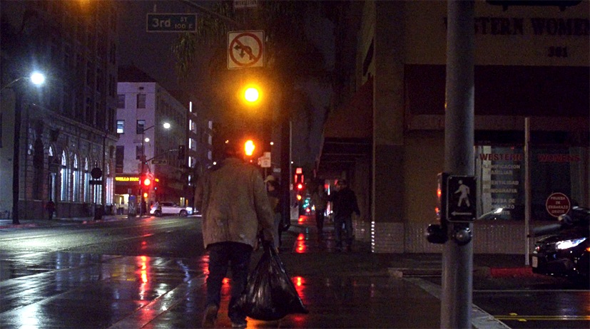 Individual walking away from camera on a dark street that is wet from the rain.