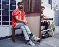 A man sitting while the artist sits  on the other side of a room divider