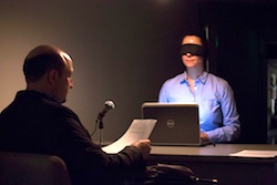 Artist Jennifer Nelson sitting, blindfolded, in front of a laptop 