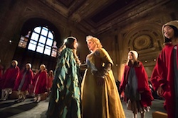 Theatrical composition of two woman in formal dresses surrounded by girls in red
