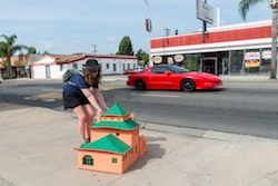 Woman carrying a cardboard house model on the sidewalk. 