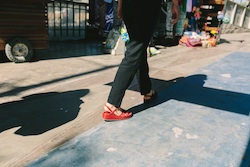 An individual wearing red wedges while walking on the street