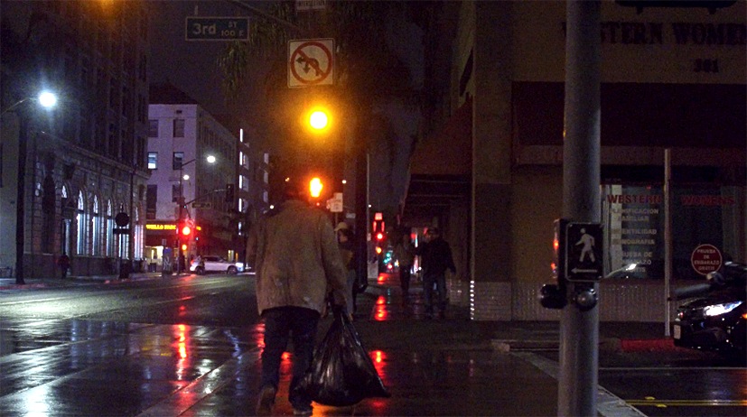 Man crossing the street carrying a trash bag. 