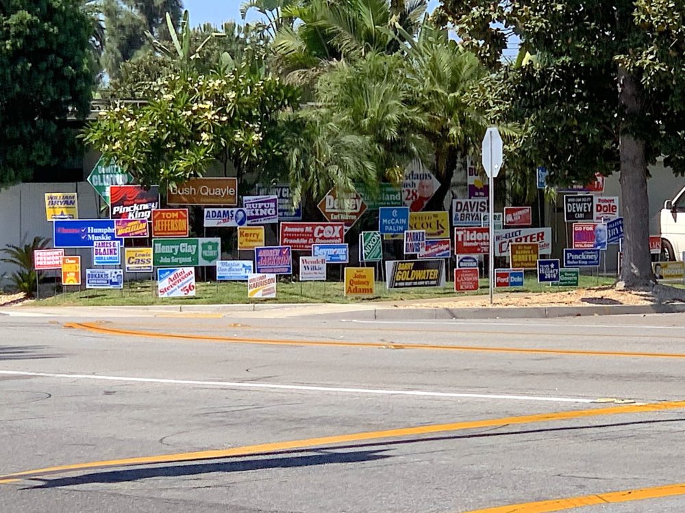 a suburban front yard with colorful elections signs that list the names of all those who ran for US president and lost