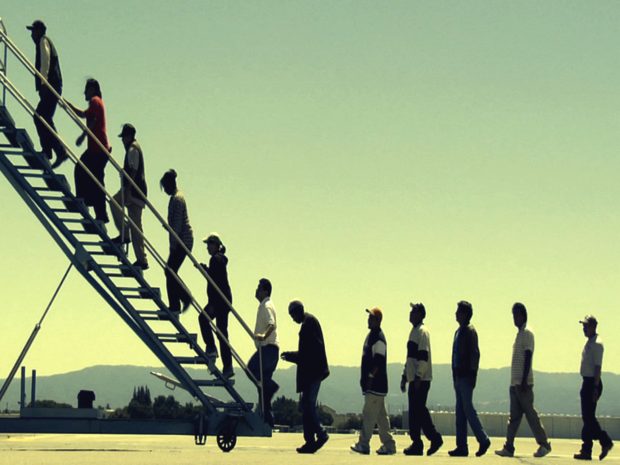 Individuals lined up walking toward and onto an airplane stairway