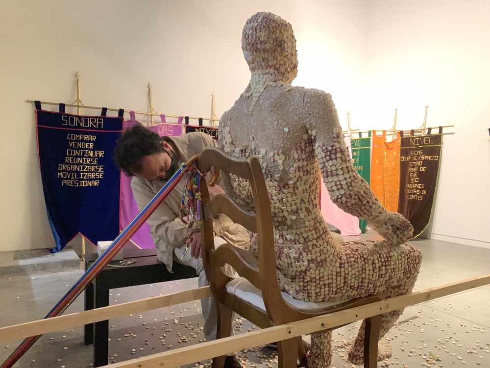 artist Alfadir Luna removing corn from his figurative sculpture corn man