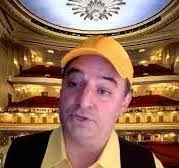 artist Pablo Helguera dressed in yellow hat, yellow shirt and brown vest with interior opera house background