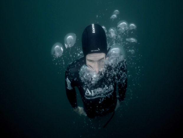 a diver underwater in a wetsuit with large bubbles surrounding their face