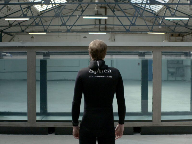 Man in wetsuit standing in front of tank filled with water.