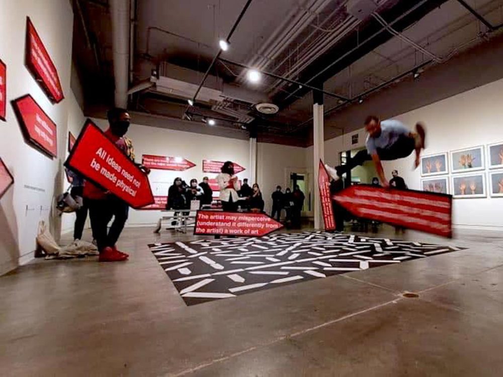 Sign spinners with red signs and white text performing movements in exhibition space