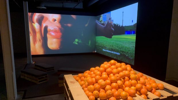 A video projection behind a pile of oranges