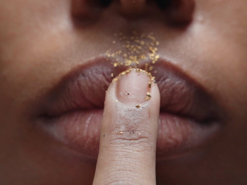 a finger with gold dust pressed against lips of a mouth.