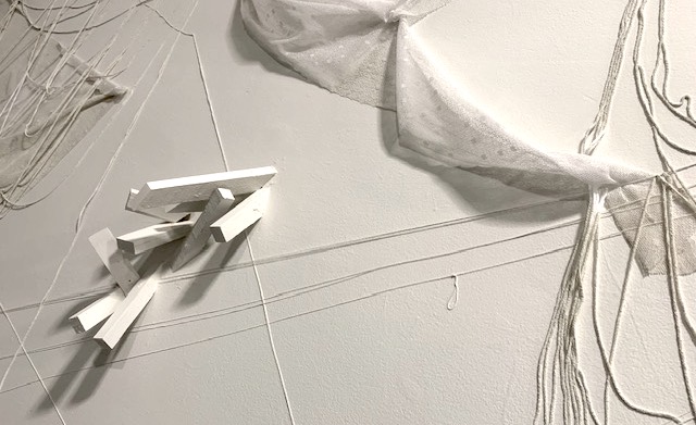 white fabric, white string, and white wood rectangles attached to white gallery wall