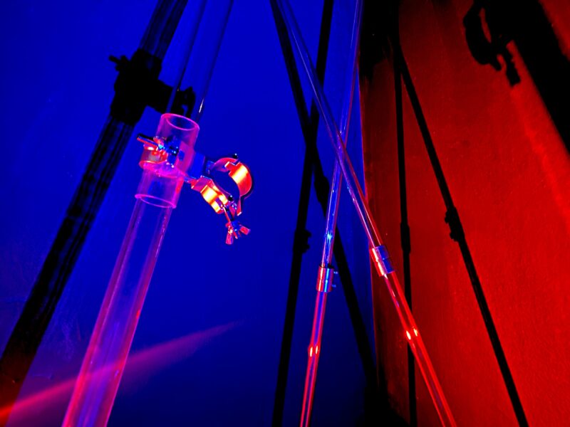 Acrylic tubes leaning against the corners of a wall with blue and red light projected upon them and the walls.